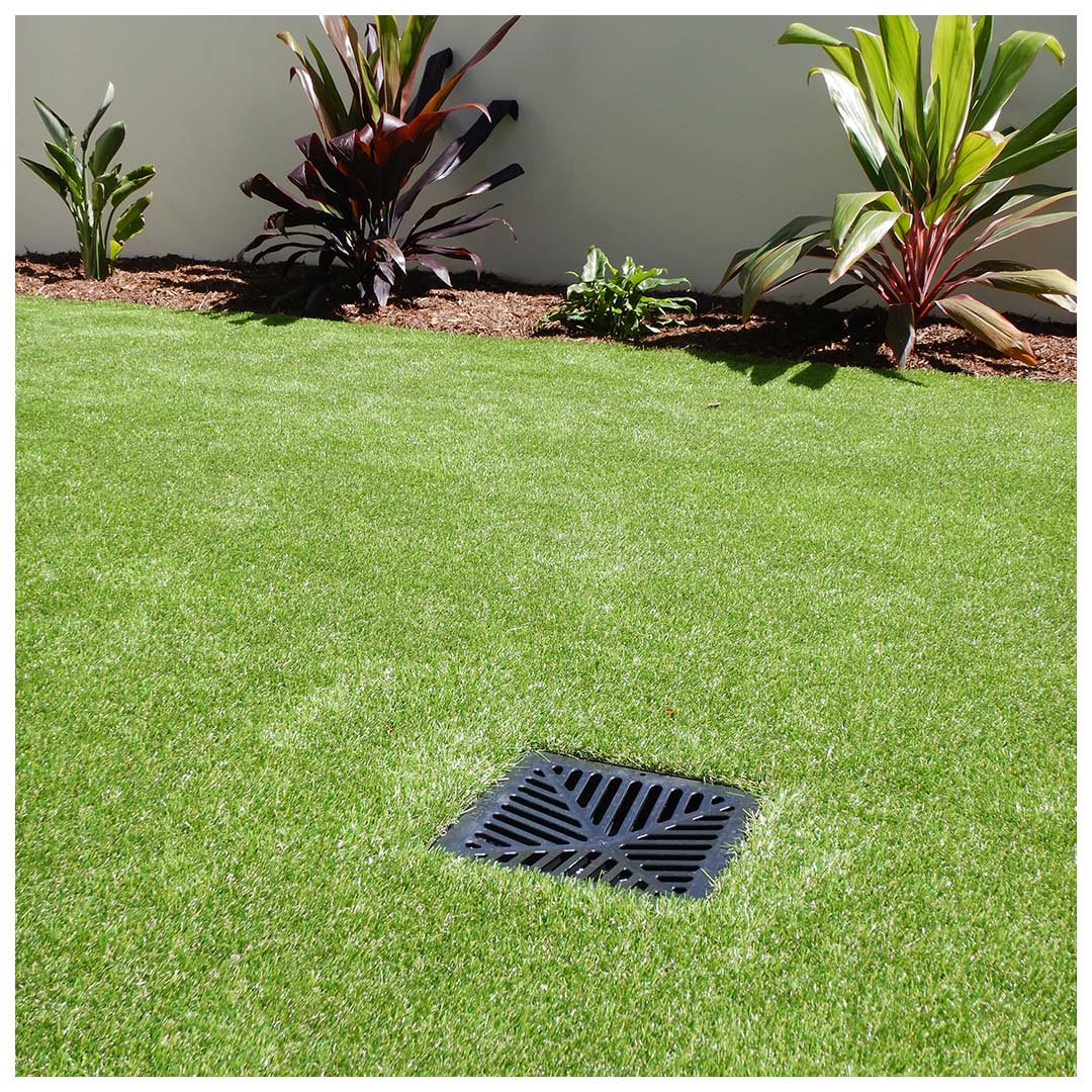 Before image of unsightly plastic drain cover surrounded by synthetic grass