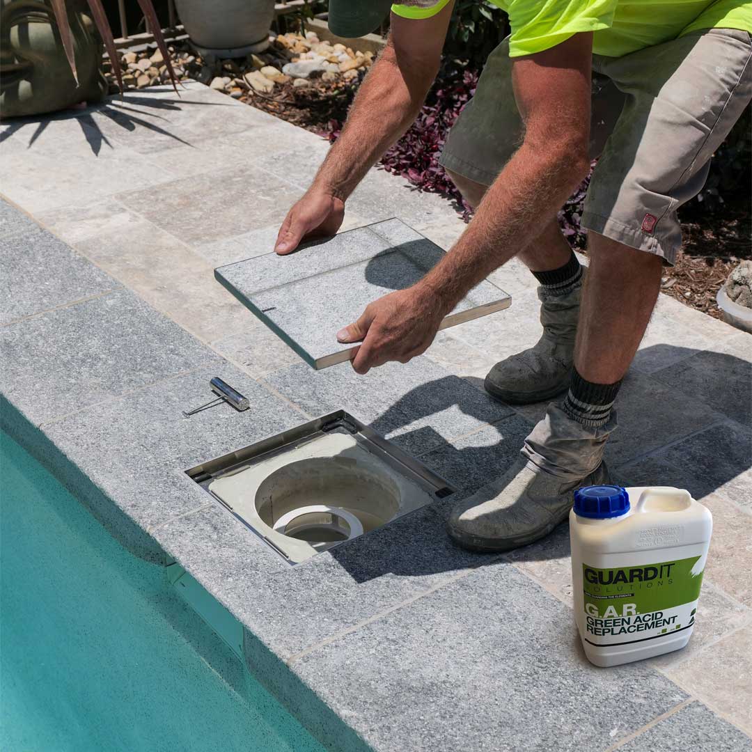 Trade cleaning HIDE Skimmer Lid with tile inlay near a pool with a bottle of 'GUARDIT' product sitting beside him.