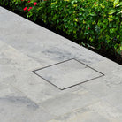 Square HIDE Drain Cover in a stone patio with greenery in the background.